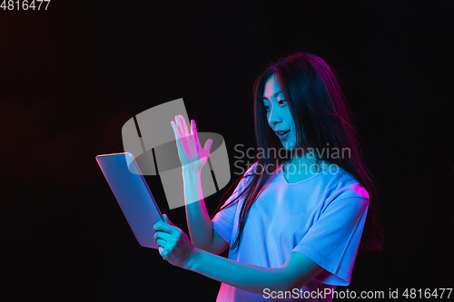 Image of Asian young woman\'s portrait on dark studio background in neon. Concept of human emotions, facial expression, youth, sales, ad.
