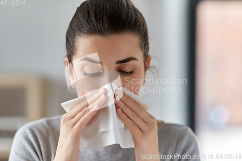 Image of sick woman blowing nose in paper tissue at home