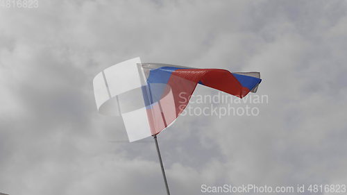 Image of Russian flag on the flagpole waving in the wind against a blue sky with clouds. Slow motion