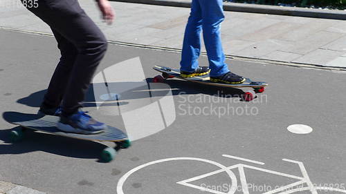 Image of Feet of two boys riding on a skateboard ride on asphalt.