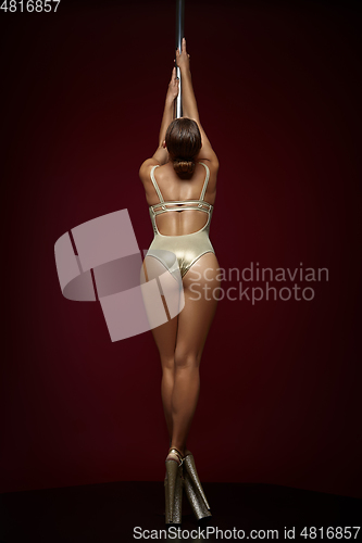 Image of beautiful pole dancer in golden bodywear on pylon