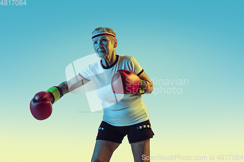 Image of Senior woman boxing in sportwear on gradient background in neon light