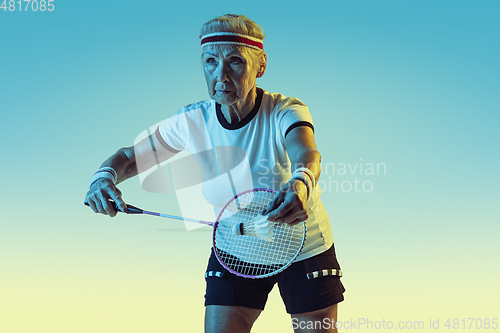 Image of Senior woman playing badminton in sportwear on gradient background in neon light