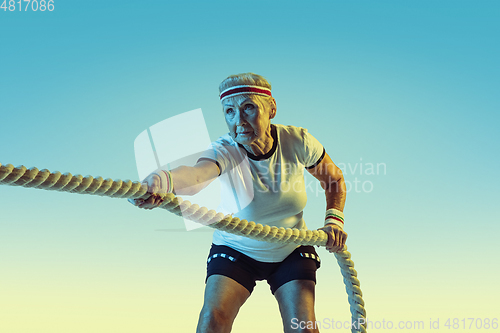 Image of Senior woman training with ropes in sportwear on gradient background in neon light