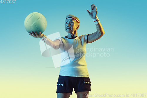 Image of Senior woman training in volleyball in sportwear on gradient background in neon light