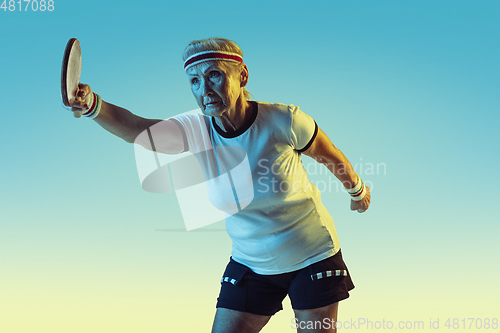 Image of Senior woman training in table tennis in sportwear on gradient background in neon light