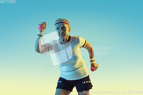 Image of Senior woman training with weights in sportwear on gradient background in neon light