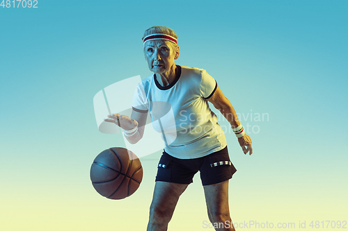 Image of Senior woman playing basketball in sportwear on gradient background in neon light