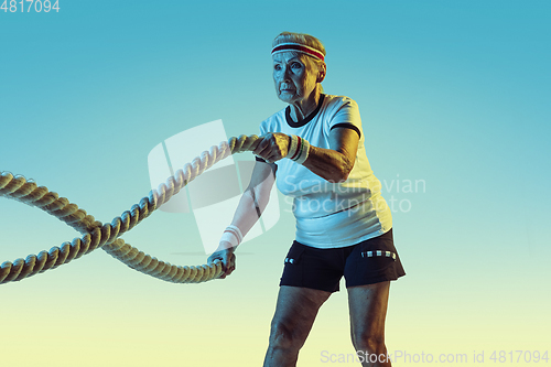 Image of Senior woman training with ropes in sportwear on gradient background in neon light