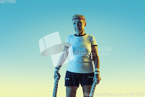 Image of Senior woman training with ropes in sportwear on gradient background in neon light