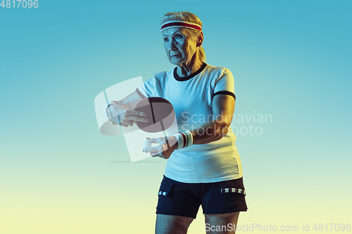 Image of Senior woman training in table tennis in sportwear on gradient background in neon light