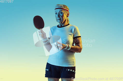 Image of Senior woman training in table tennis in sportwear on gradient background in neon light