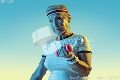 Image of Senior woman training with weights in sportwear on gradient background in neon light