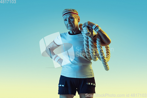 Image of Senior woman training with ropes in sportwear on gradient background in neon light