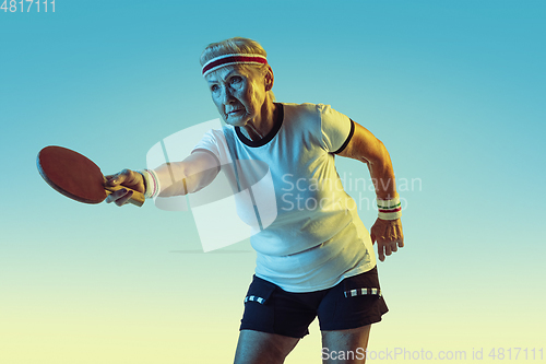 Image of Senior woman training in table tennis in sportwear on gradient background in neon light