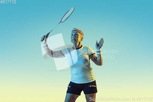 Image of Senior woman playing badminton in sportwear on gradient background in neon light