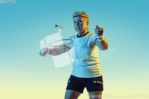 Image of Senior woman playing badminton in sportwear on gradient background in neon light