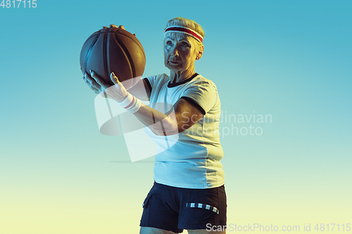 Image of Senior woman playing basketball in sportwear on gradient background in neon light