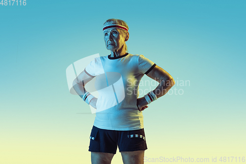 Image of Senior woman training and posing in sportwear on gradient background in neon light