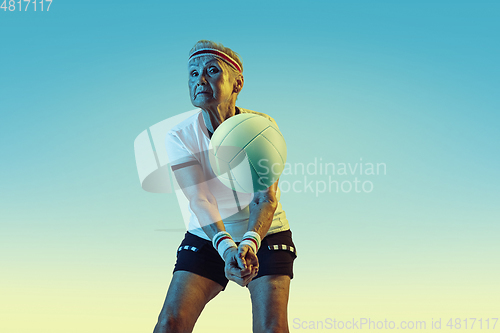 Image of Senior woman training in volleyball in sportwear on gradient background in neon light