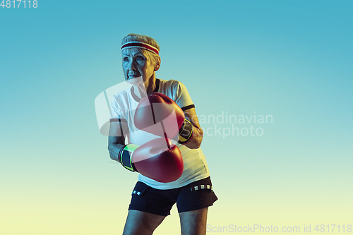 Image of Senior woman boxing in sportwear on gradient background in neon light