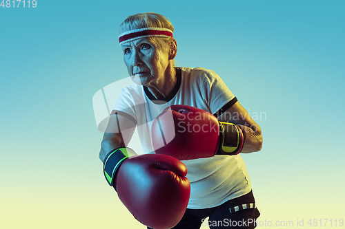 Image of Senior woman boxing in sportwear on gradient background in neon light