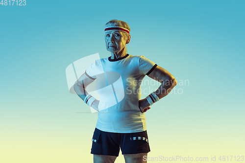 Image of Senior woman training and posing in sportwear on gradient background in neon light