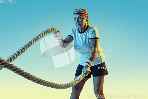 Image of Senior woman training with ropes in sportwear on gradient background in neon light