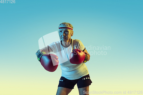 Image of Senior woman boxing in sportwear on gradient background in neon light