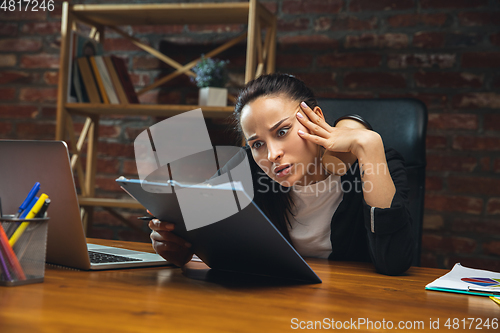 Image of Young woman working in modern office using devices and gadgets. Making reports, analitycs, routine processing tasks