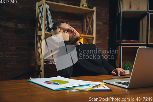 Image of Young man working in modern office using devices and gadgets. Making reports, analitycs, routine processing tasks