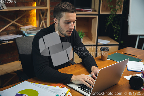 Image of Young man working in modern office using devices and gadgets. Making reports, analitycs, routine processing tasks
