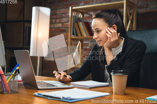 Image of Young woman working in modern office using devices and gadgets. Making reports, analitycs, routine processing tasks