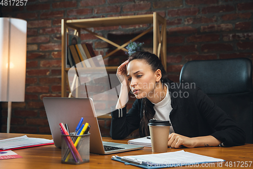 Image of Young woman working in modern office using devices and gadgets. Making reports, analitycs, routine processing tasks