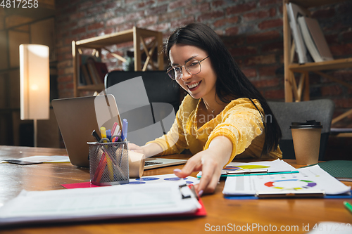 Image of Young woman working in modern office using devices and gadgets. Making reports, analitycs, routine processing tasks