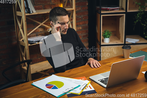 Image of Young man working in modern office using devices and gadgets. Making reports, analitycs, routine processing tasks