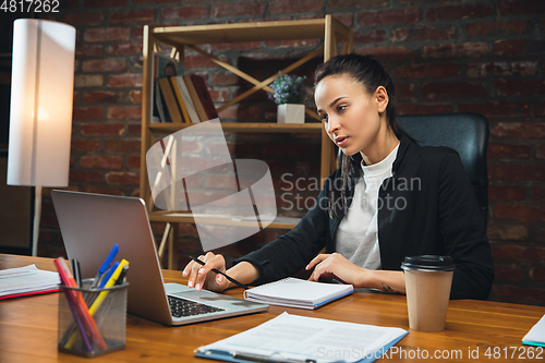 Image of Young woman working in modern office using devices and gadgets. Making reports, analitycs, routine processing tasks