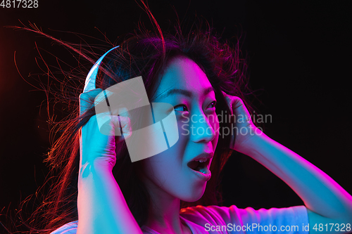 Image of Asian young woman\'s portrait on dark studio background in neon. Concept of human emotions, facial expression, youth, sales, ad.