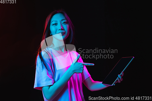 Image of Asian young woman\'s portrait on dark studio background in neon. Concept of human emotions, facial expression, youth, sales, ad.