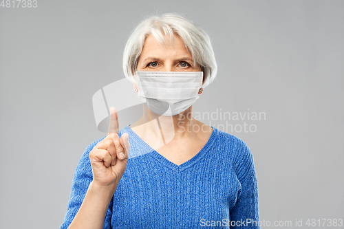 Image of senior woman in medical mask pointing finger up