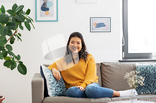 Image of smiling asian young woman sitting on sofa at home