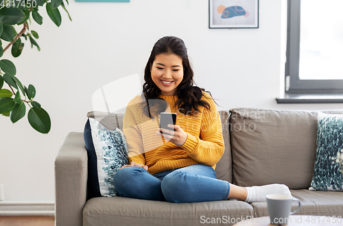 Image of happy asian young woman with smartphone at home