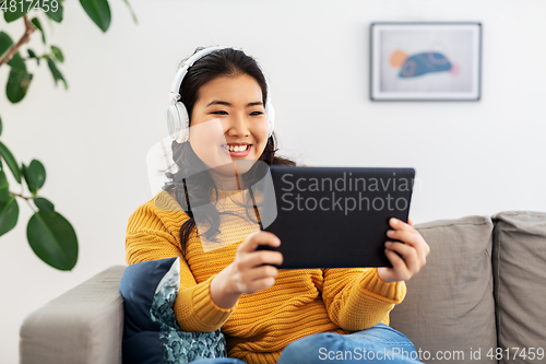 Image of asian woman with headphones and tablet pc at home