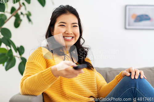 Image of asian woman with tv remote sitting on sofa at home