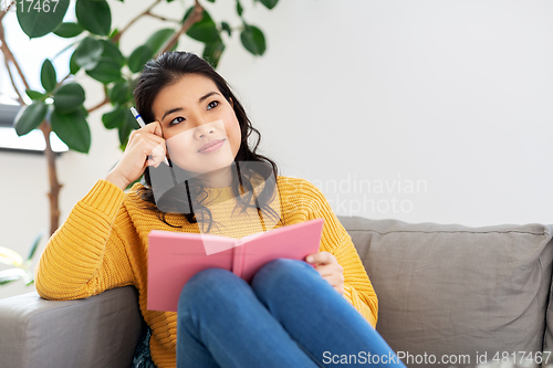 Image of asian woman with diary sitting on sofa at home