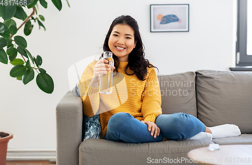 Image of smiling asian young woman drinking water at home