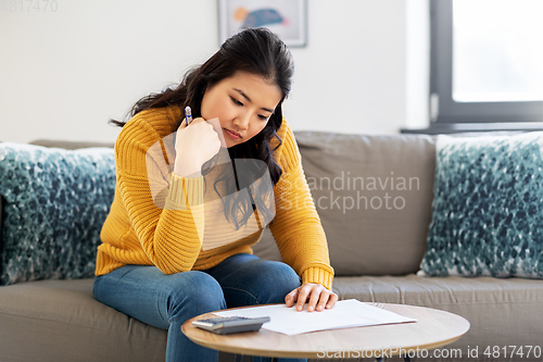 Image of sad asian woman with papers and calculator at home