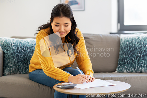 Image of asian woman with papers and calculator at home