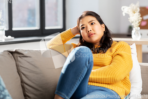 Image of worried asian young woman sitting on sofa at home