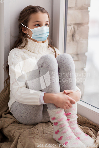 Image of sad girl in medical mask sitting on sill at home